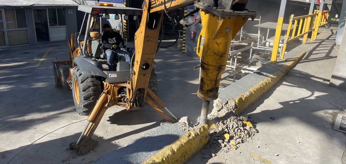 Retroexcavadora con martillo demoliendo concreto dentro de una planta industrial